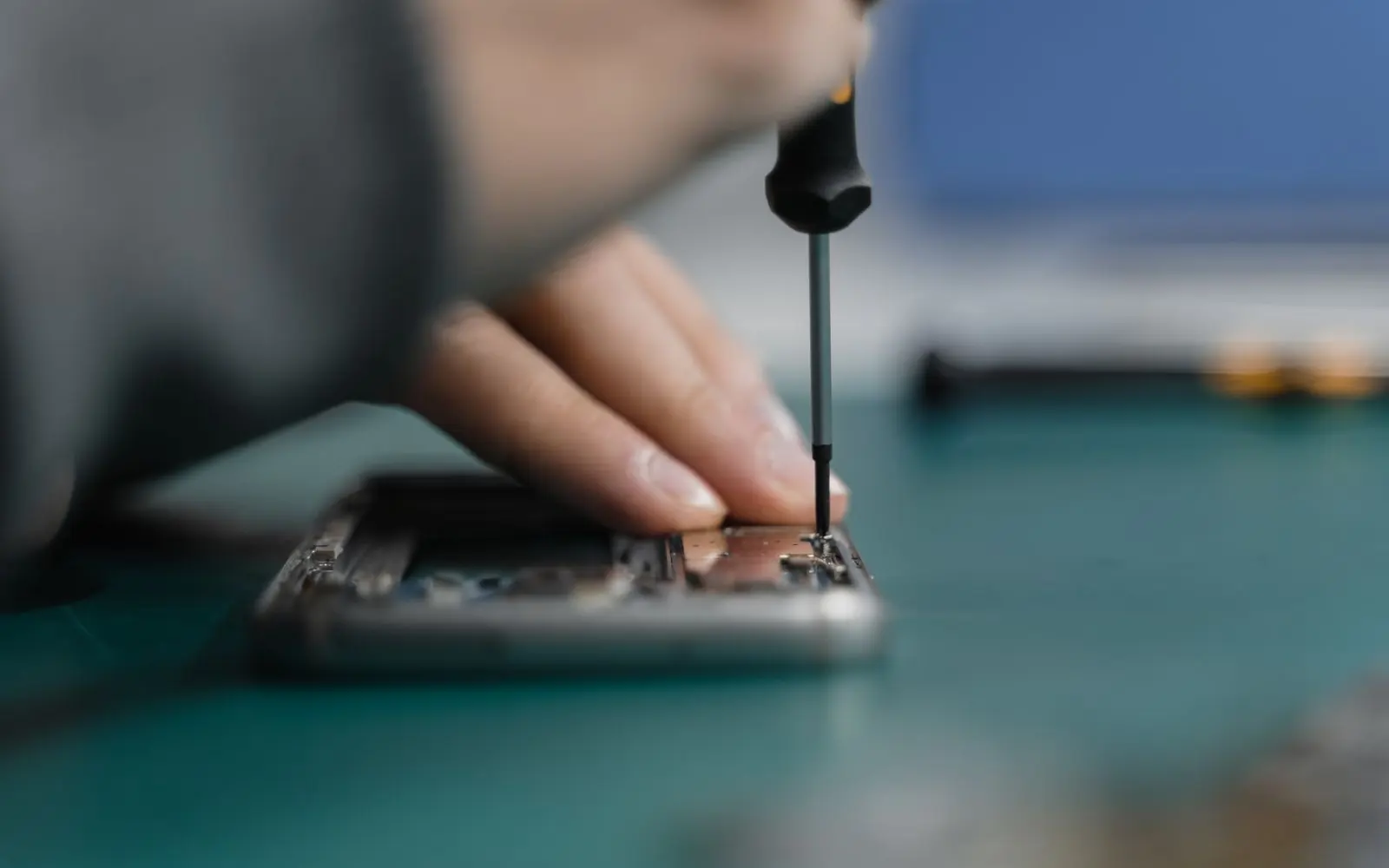 Main d’un technicien démontant un appareil au tournevis sur un tapis d’atelier